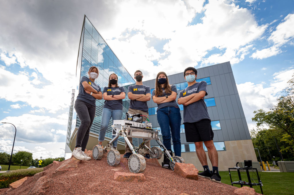 A team of students standing behind a rover on a mars-like hill