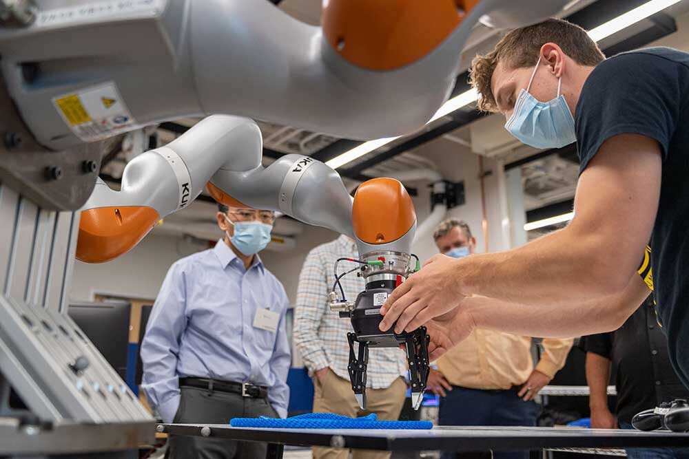 A robot arm grasps a rope as a researcher assists.