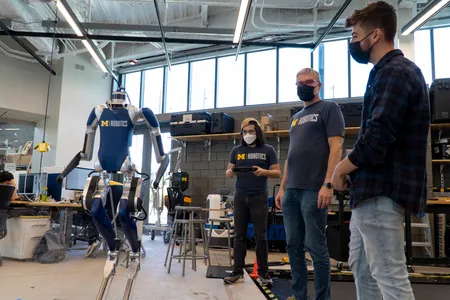 Professor Jessy Grizzle shows Victor Popa-Simil a Cassie robot with a lidar sensor on top.