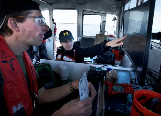 Two researchers on a boat, as one of them points to the sonar data they are collecting on a screen.