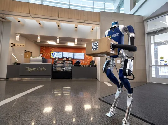 A Digit bipedal robot holds a package in the lobby of the Robotics Building at the University of Michigan.