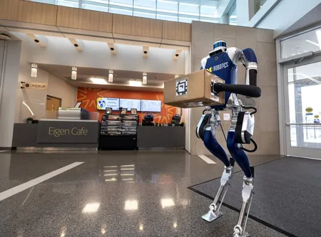 A Digit bipedal robot holds a package in the lobby of the Robotics Building at the University of Michigan.