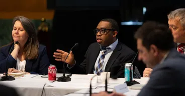 A group at a conference table with a man speaking and gesturing.
