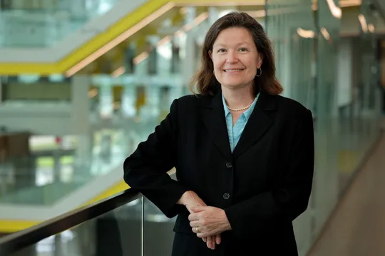 Dawn Tilbury smiles while leaning on a glass railing in the atrium of the Ford Robotics Building.