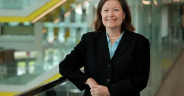 Dawn Tilbury smiles while leaning on a glass railing in the atrium of the Ford Robotics Building.