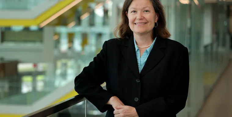 Dawn Tilbury smiles while leaning on a glass railing in the atrium of the Ford Robotics Building.