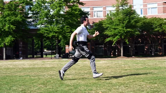 Legs of a user walking on a two-track treadmill in a lab wearing powered ankle exoskeletons.