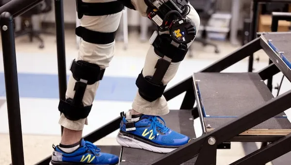 A researcher wearing motorized knee exoskeletons on both legs ascends a flight of stairs.