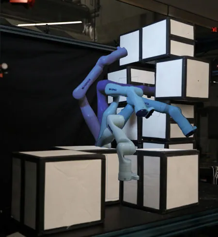 Three overlaid color-coded trajectories of a robot arm reaching through a cluttered stack of boxes on a workbench.