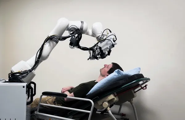A research subject reclined on an exam bed with the eye imaging machine held in the proper place with a robot arm.