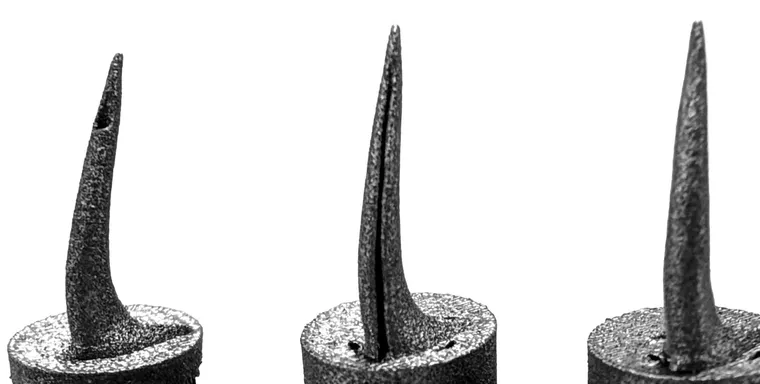 Three 3D-printed titanium snake fangs side by side, each with a different venom channel structure, mounted on cylindrical bases.