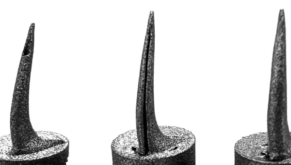Three 3D-printed titanium snake fangs side by side, each with a different venom channel structure, mounted on cylindrical bases.