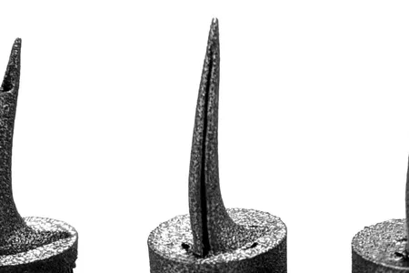 Three 3D-printed titanium snake fangs side by side, each with a different venom channel structure, mounted on cylindrical bases.