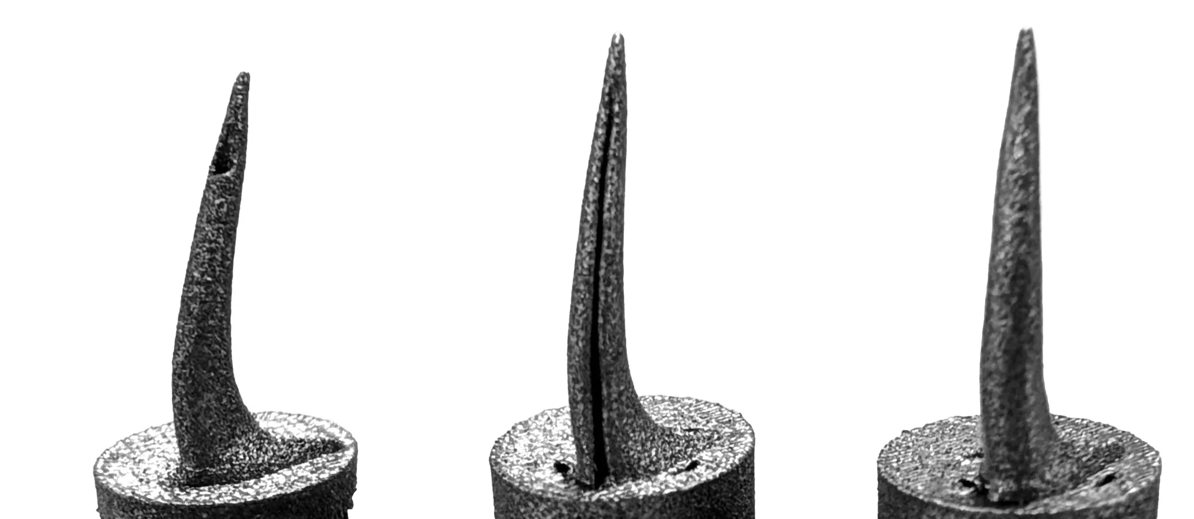 Three 3D-printed titanium snake fangs side by side, each with a different venom channel structure, mounted on cylindrical bases.