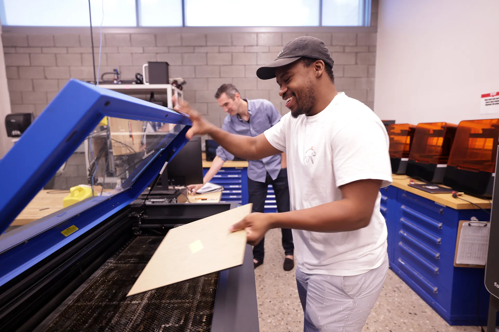 A student loads a sheet of metal in to a laser cutter in the Makerspace