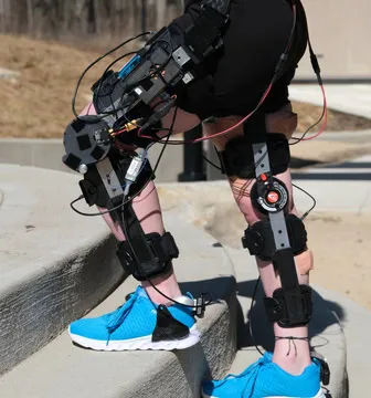 A person wearing a knee exo standing across stairs outside.