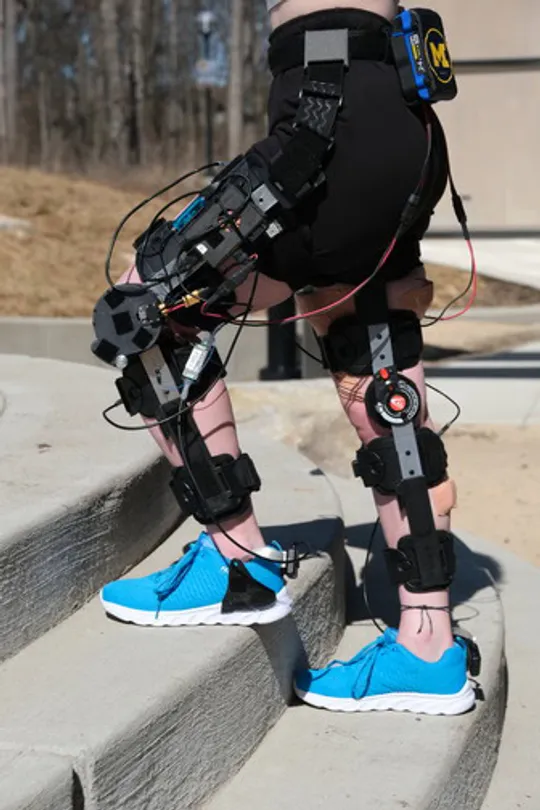 A person wearing a knee exo standing across stairs outside.