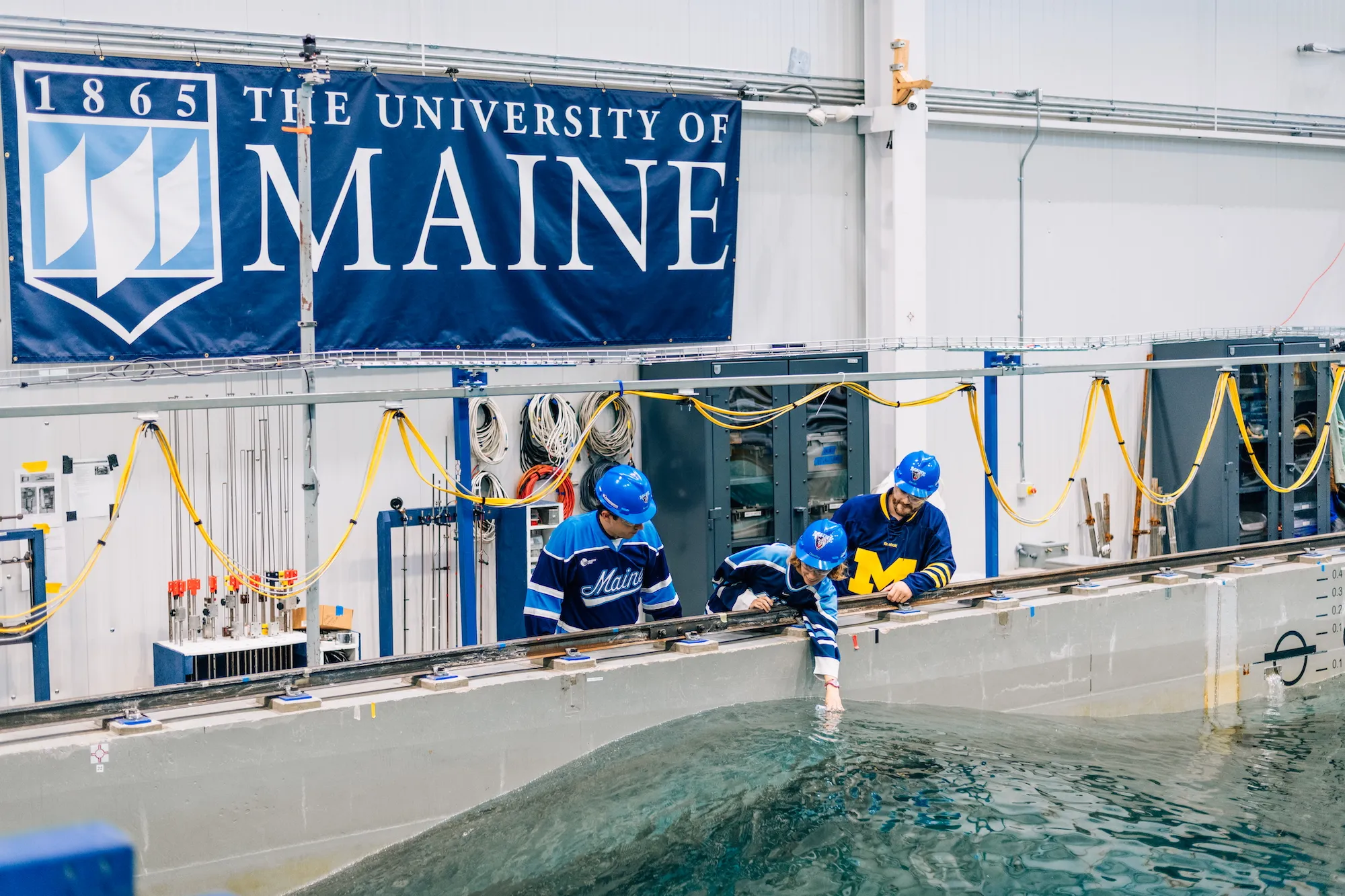 Three researchers at Maine's research water tank collect a water sample at the crest of a large wave.