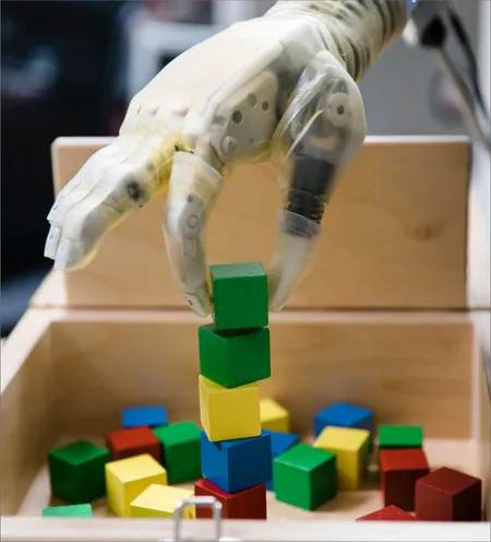 Close up of advanced prosthetic hand with a green block grasped between the thumb and index finger, positioning the block at the top of a stack.