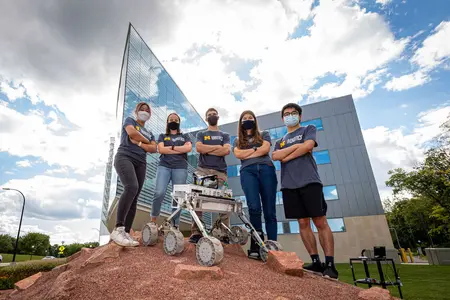 Five Michigan Robotics students pose with the MRover robot at the Ford Robotics Building Mars Yard
