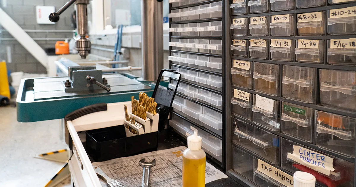 A collection of tools and drill bits in front of a drill press