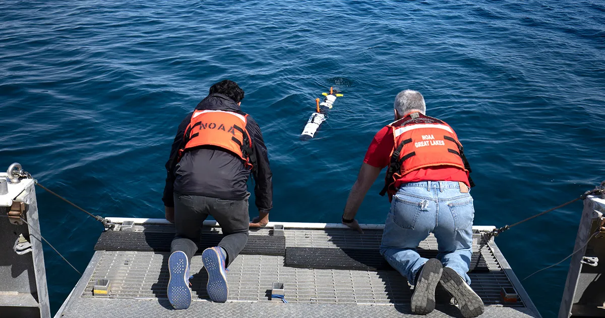 An underwater robot on the surface of a lake is retrieved by two researchers.