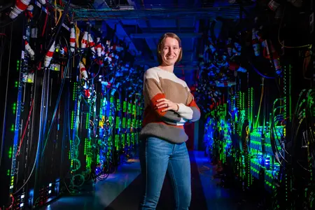 A researcher stands in a server room illuminated by green LED lights