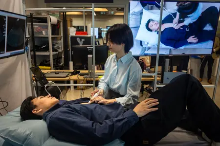 A researcher performs a robotic ultrasound procedure while screens display imaging results