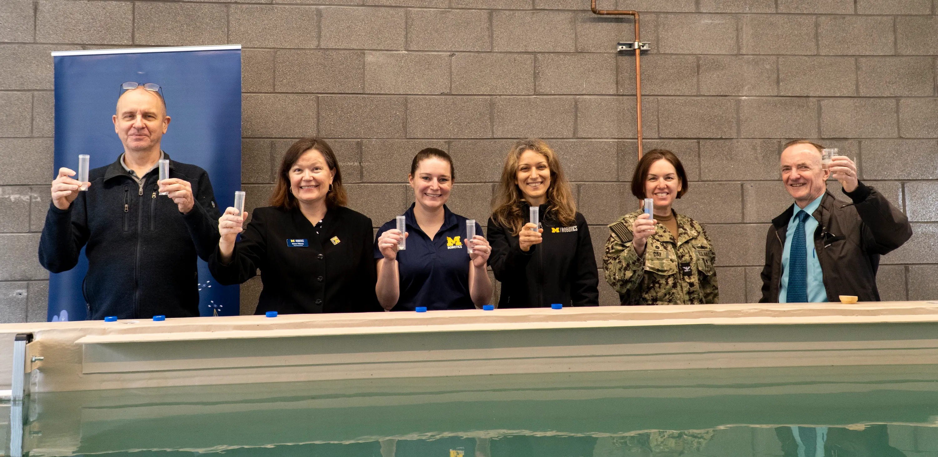 A group holds up water samples from around the country that will be poured into the new water research tank.