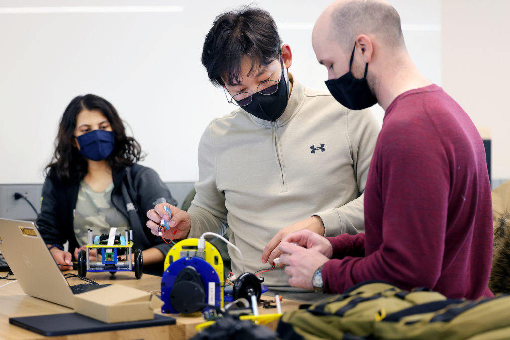Three students work on a small mobile robot on a workbench. Photo: Brenda Ahearn