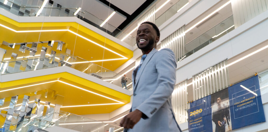 A student smiles with the iconic yellow staircase of the Robotics Building in the background.
