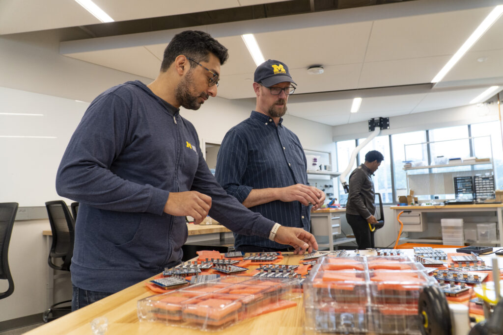 Abhishek Narula and Peter Gaskell sort through a table of Mbot PICO+ chips in the ROB 550 lab.