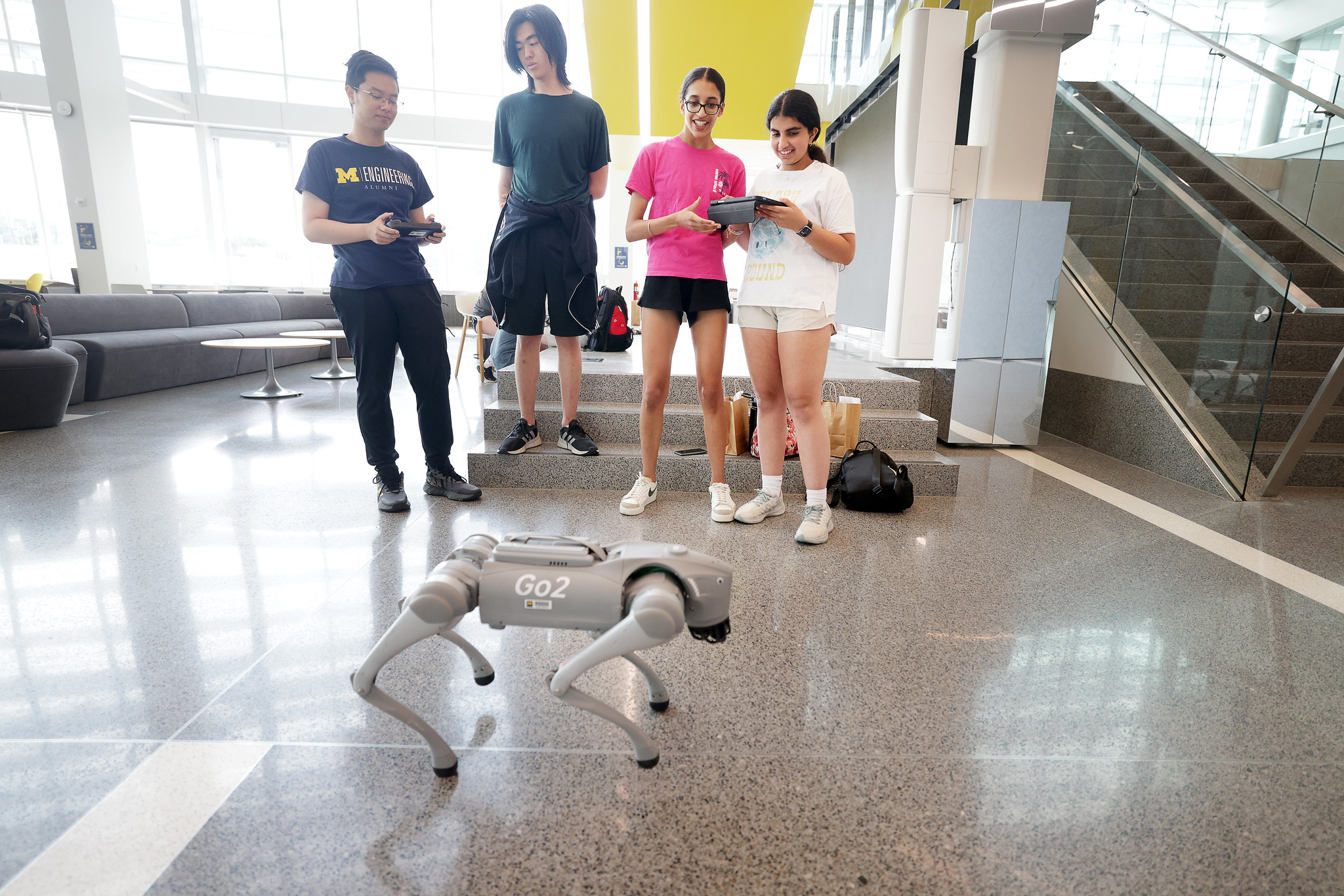 Two camp counselors and two summer campers stand in front of a quadruped robot in the Ford Robotics Building.